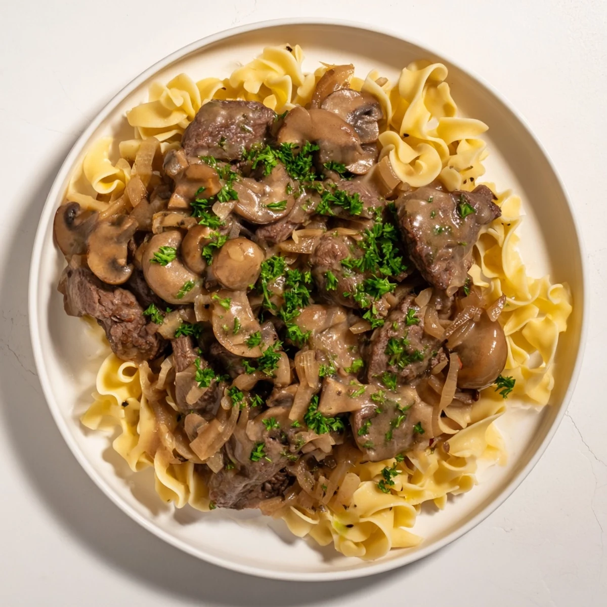 A close-up of Creamy Mushroom Beef Stroganoff, showing the glistening beef and sauce over fluffy egg noodles.