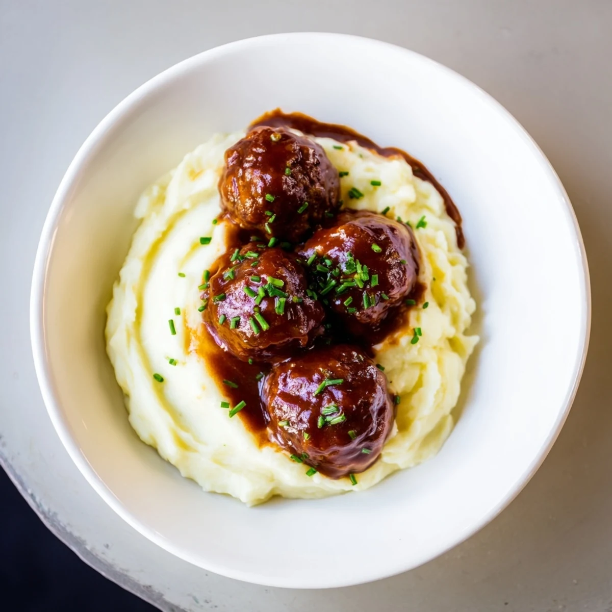 Juicy BBQ meatballs glistening with sauce, resting atop a bed of creamy, buttery mashed potatoes.