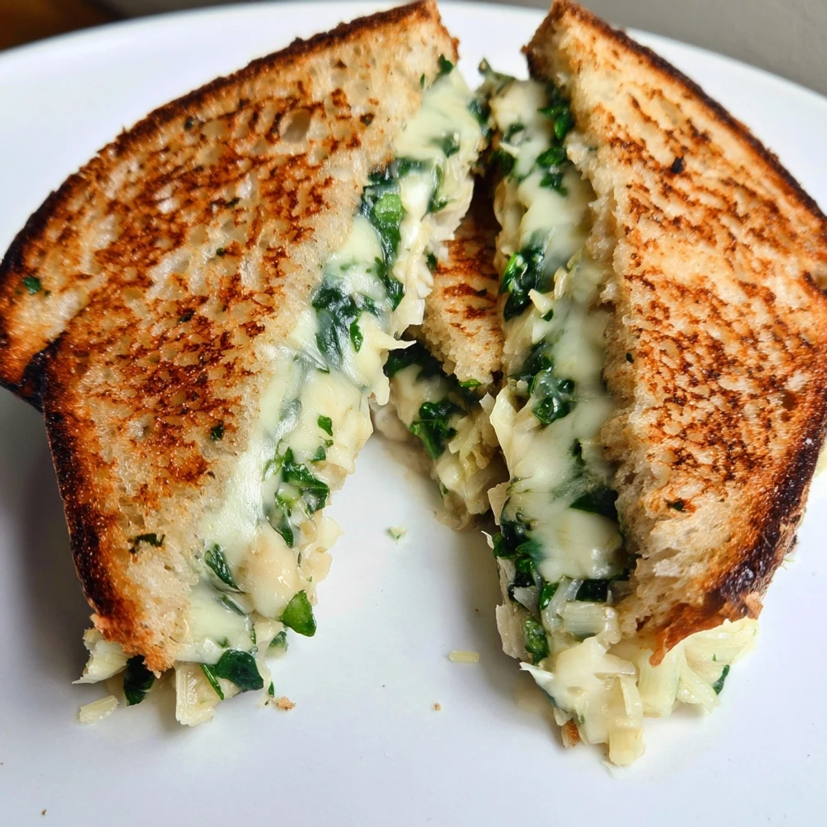 A fork cutting into an Artichoke Spinach Grilled Cheese, revealing a thick, creamy dip-style filling with vibrant green spinach and tender artichokes.