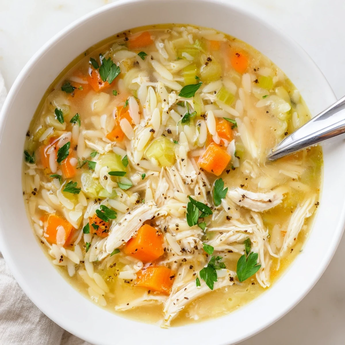 A steaming bowl of Lemon Pepper Chicken Orzo Soup with tender shredded chicken, bright lemon zest, and orzo pasta, garnished with fresh parsley and black pepper.