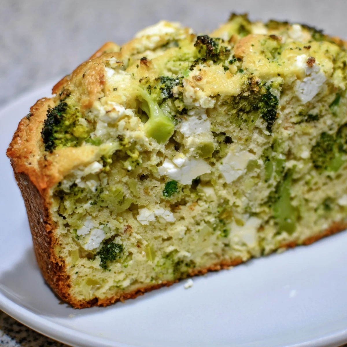 Warm loaf of Broccoli and Feta Loaf resting on a wire rack, steam rising from the moist, tender interior speckled with savory feta and broccoli.  