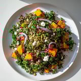 A close-up shot of the fresh Kale & Quinoa Salad, featuring sweet potato chunks and bright pomegranate seeds.