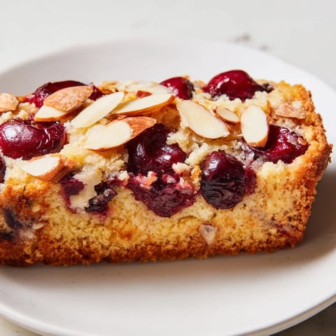 Golden, sliced Cherry Almond Loaf Cake, showcasing juicy cherries and crunchy almond topping.