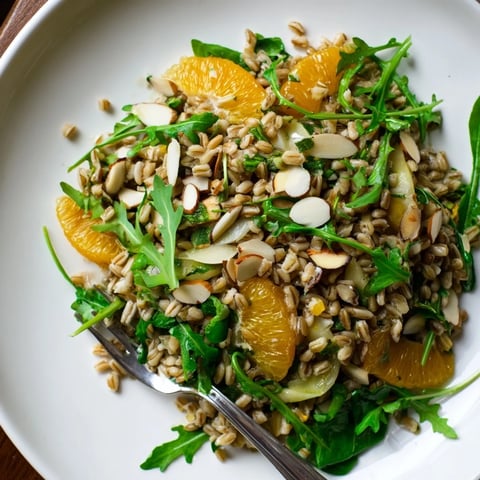 Farro Salad With Fennel, Oranges, and Almonds glistens in a white bowl, featuring chewy grains, crisp fennel shavings, bright orange segments, and toasted almonds over arugula.