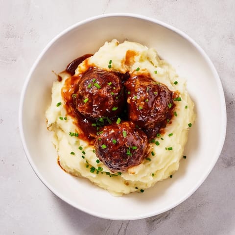 Hearty BBQ meatballs over fluffy mashed potatoes, topped with fresh herbs, a delicious weeknight dinner.