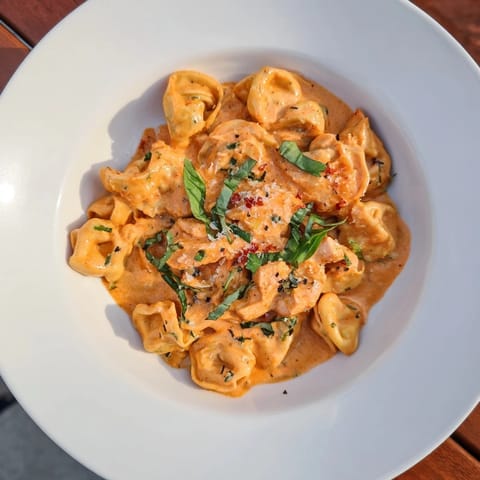 A close-up shot of the Marry Me Chicken Tortellini, garnished with fresh basil and Parmesan.