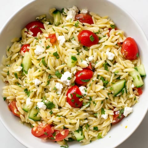 Greek Orzo Salad served in a white bowl with a zesty lemon-oregano dressing, fresh parsley, and red onion slices for a Mediterranean side.  