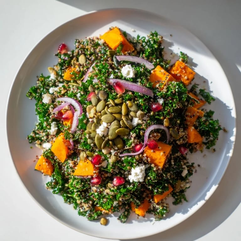 A close-up shot of the fresh Kale & Quinoa Salad, featuring sweet potato chunks and bright pomegranate seeds.