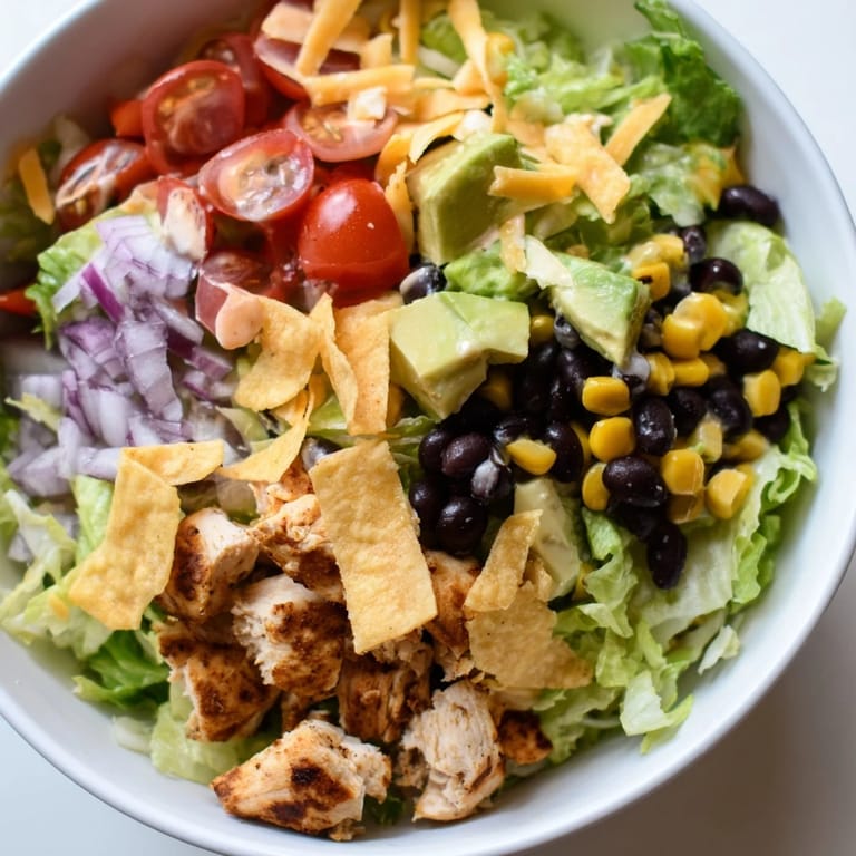 A generous handful of crushed tortilla chips and creamy avocado add texture to the vibrant Chicken Taco Chopped Salad, finished with a drizzle of salsa ranch dressing.  