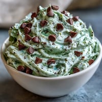 Creamy green mint chocolate chip dip served in a festive bowl, perfect for St. Patrick's Day celebrations with graham crackers and fresh fruit.